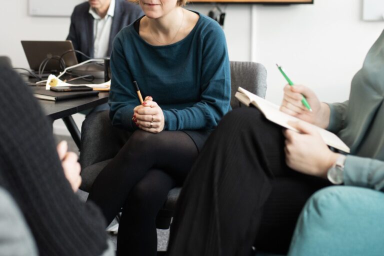 Personer som sitter i ett mötesrum och håller anteckningsböcker