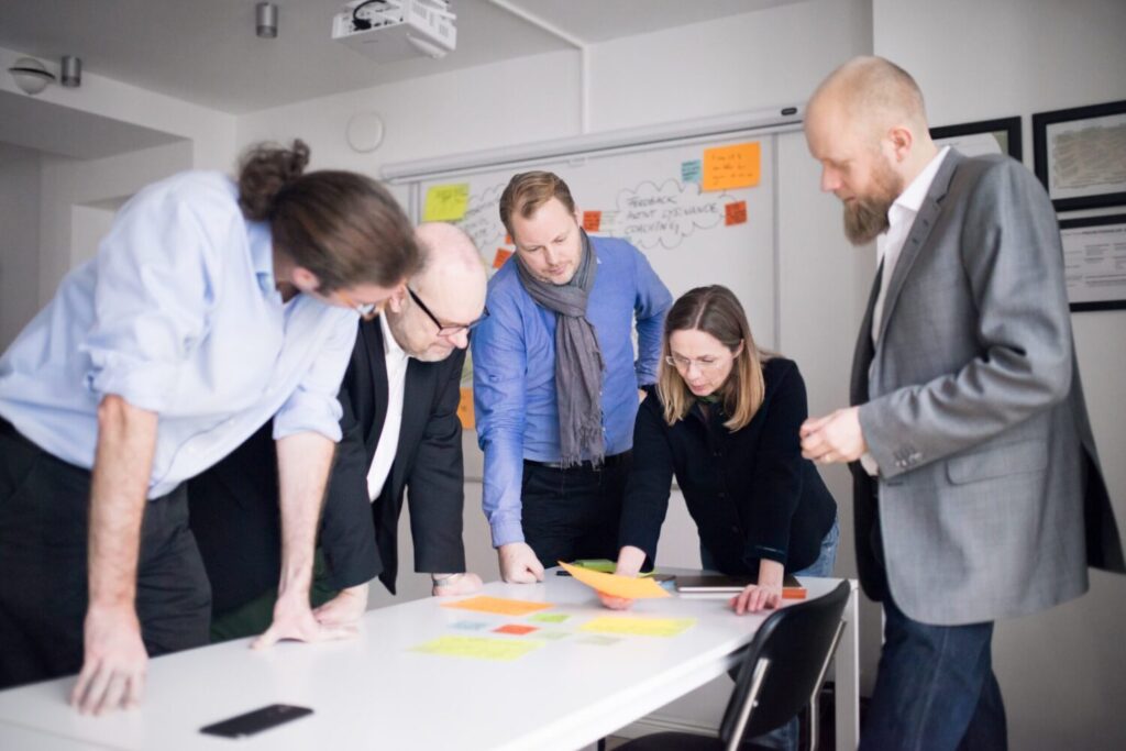 Fem personer som står och blickar ned på massa post-it lappar