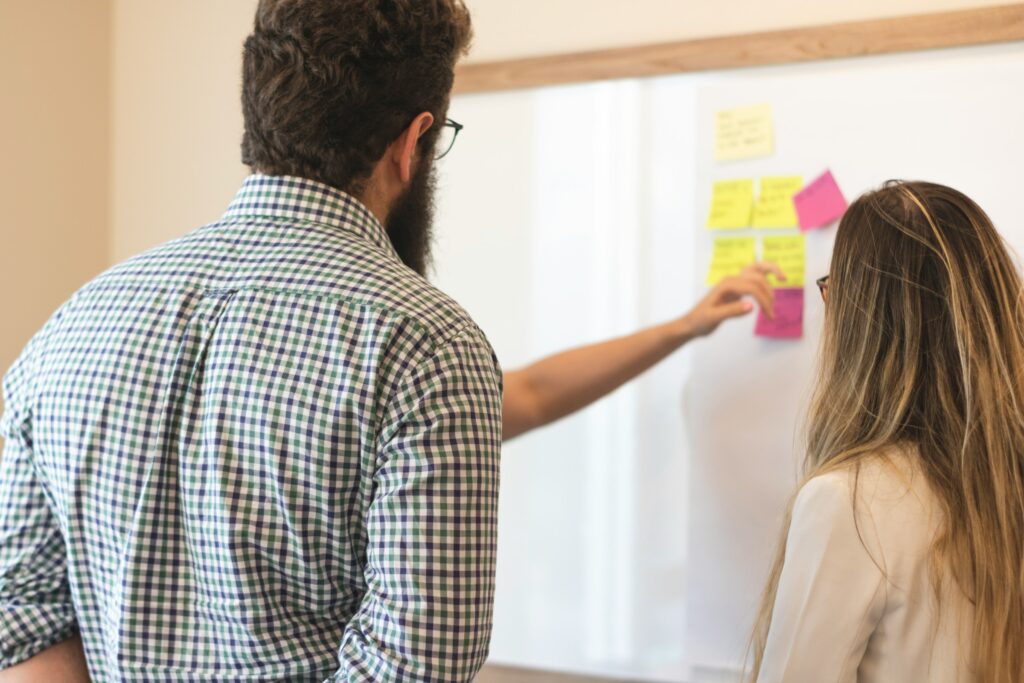 En man och en kvinna som står framför en tavla med post-it lappar på